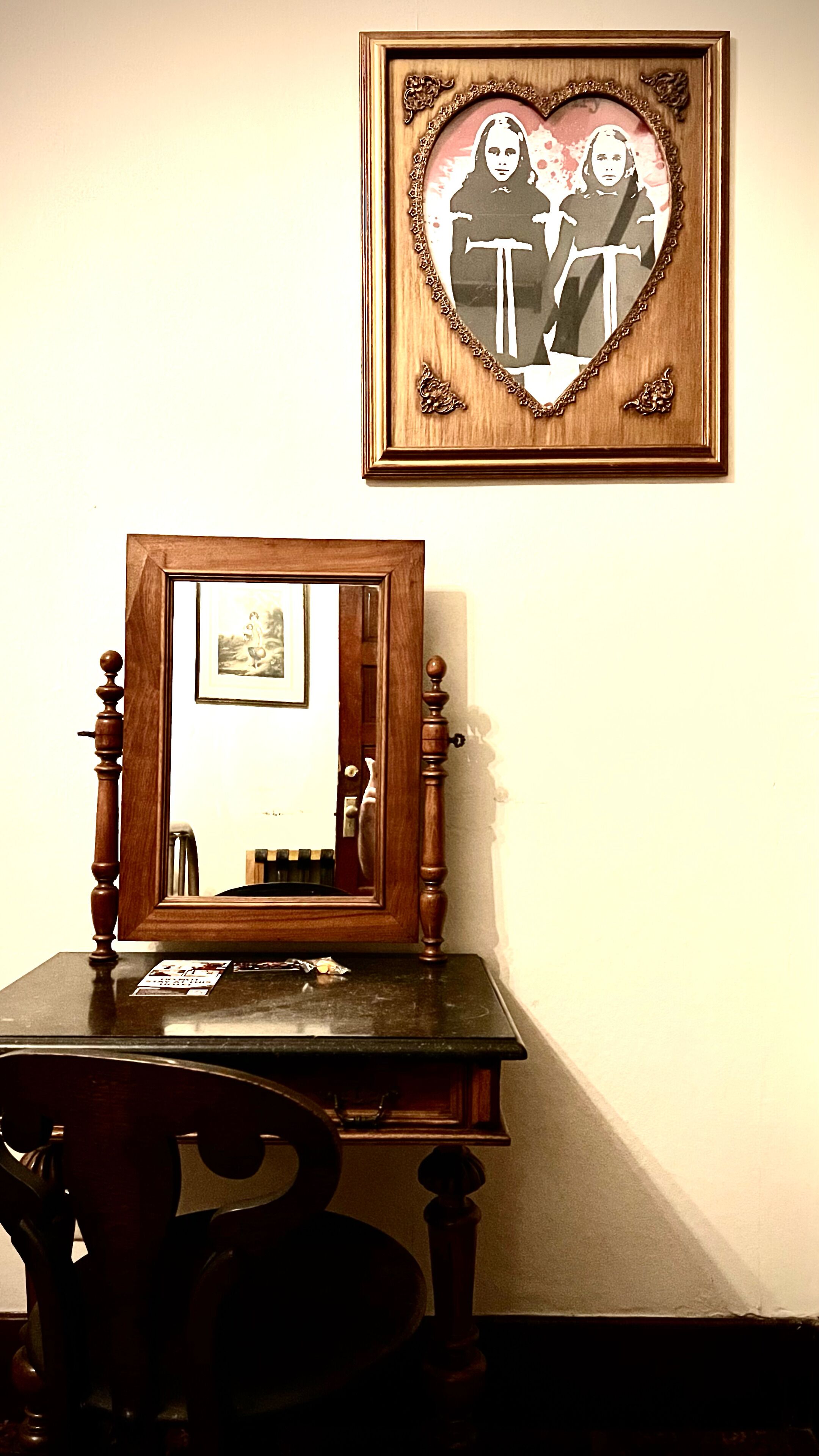 Une pièce avec un bureau en bois, une chaise, un miroir encadré et un tableau encadré accroché au mur.