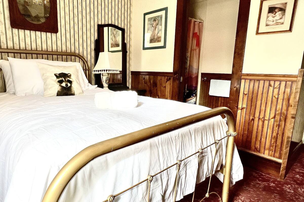 A bed with a metal frame, white bedding, and a raccoon pillow. There are framed pictures on the wall and a wooden door.