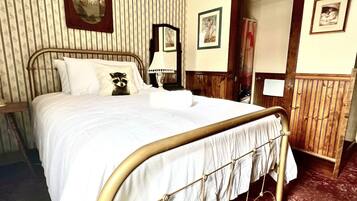 A bed with a metal frame, white bedding, and a raccoon pillow. There are framed pictures on the wall and a wooden door.