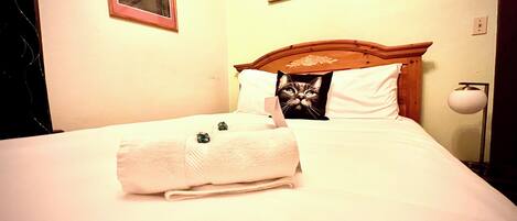 A neatly made bed with a folded white towel and a pillow with a cat image.