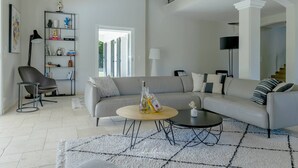 A modern living room with a grey sofa, a round coffee table, a bookshelf, and a staircase leading to an upper level.