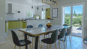 A modern kitchen with a dining area, featuring a large island, pendant lights, and a view of the outdoors.