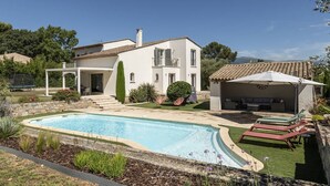 A two-story house with a swimming pool, a covered outdoor seating area, and a garden with various plants.