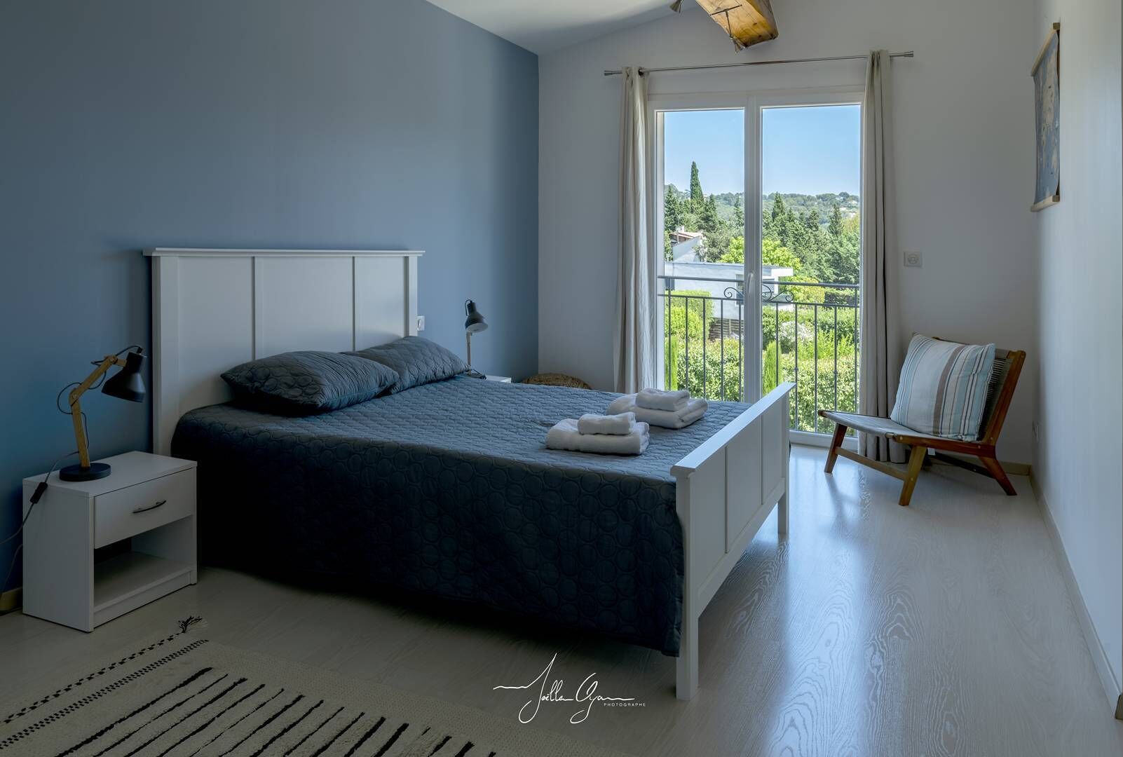 Ein Schlafzimmer mit Bett, Nachttisch, Lampe und Blick ins Grüne durch ein Fenster.