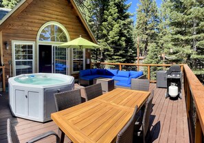 A wooden deck with a hot tub, a wooden table, and blue seating. - Alpen Glow By Tahoe Getaways Luxury 3 BR Hot tub Easy Walk to Lake (Carnelian Bay)