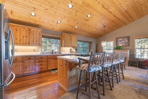 A kitchen with wooden cabinets, a stainless steel refrigerator, and a bar area with wooden chairs.
