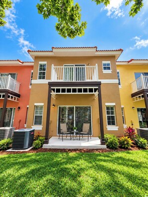 A two-story residential building with a balcony, a patio with chairs, and a small garden area.