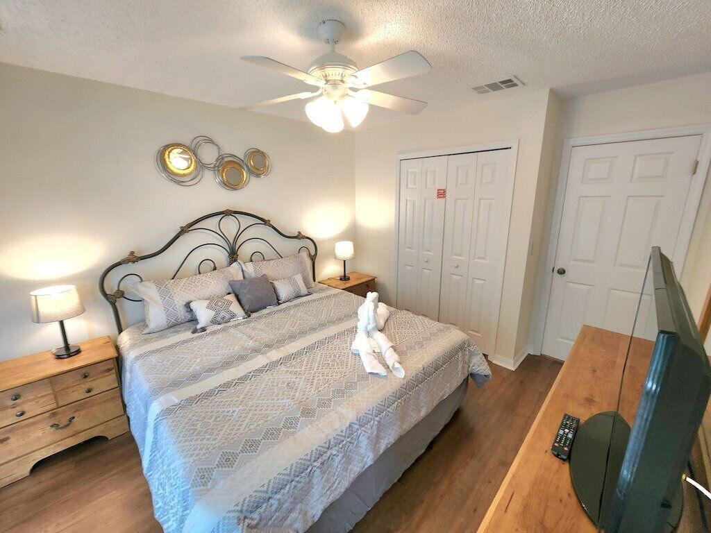 Ein Schlafzimmer mit Bett, Nachttischlampen, Deckenventilator, Fernseher und Kleiderschrank.
