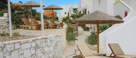 A resort with stone walls, wooden lounge chairs, and thatched umbrellas.