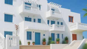 Un edificio blanco de varios pisos con detalles azules, balcones y plantas en macetas.