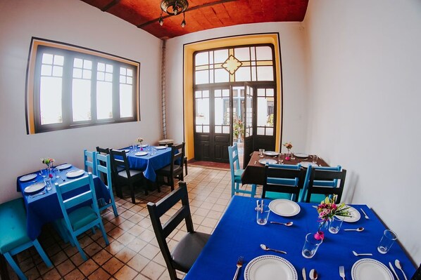 Comedor con mesas dispuestas para cuatro, manteles azules y sillas.