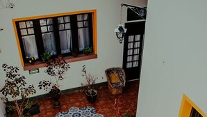 Una escalera conduce a un patio empedrado con plantas en macetas, un tapete estampado y muebles de mimbre.