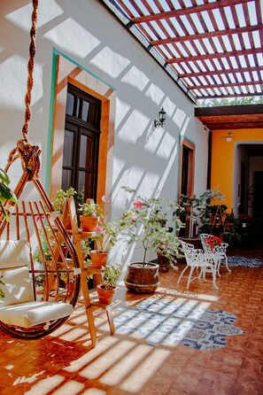 Un patio soleado con una hamaca de madera, plantas en macetas y suelo de baldosas.