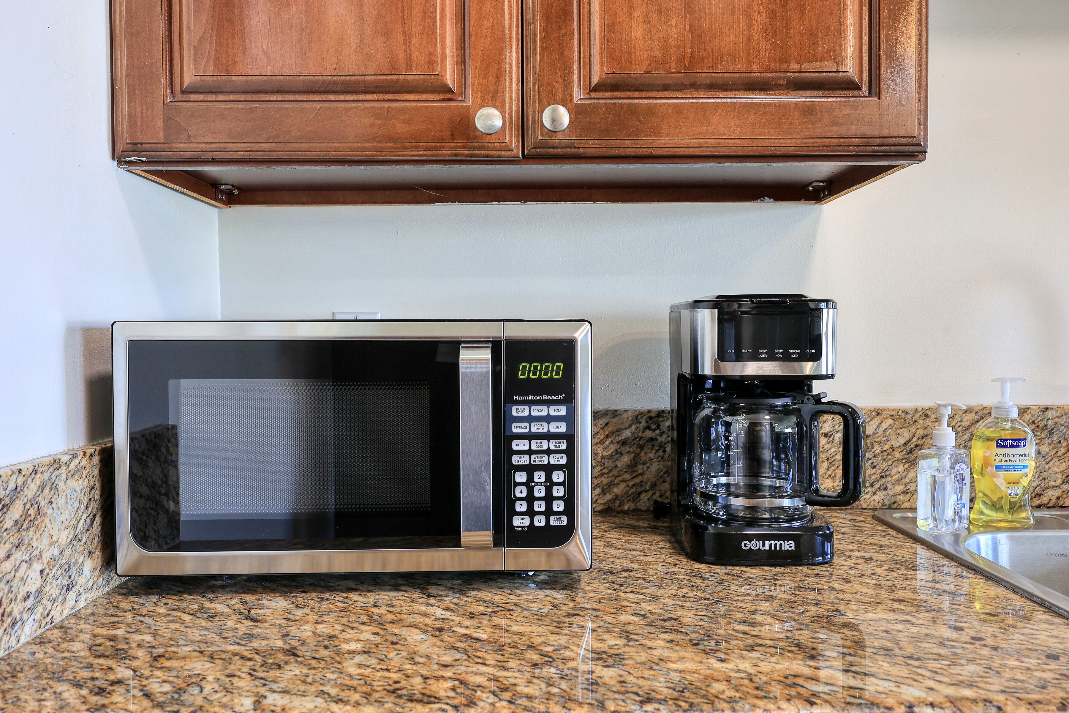 A kitchen with a microwave, coffee maker, and soap dispenser on the counter.