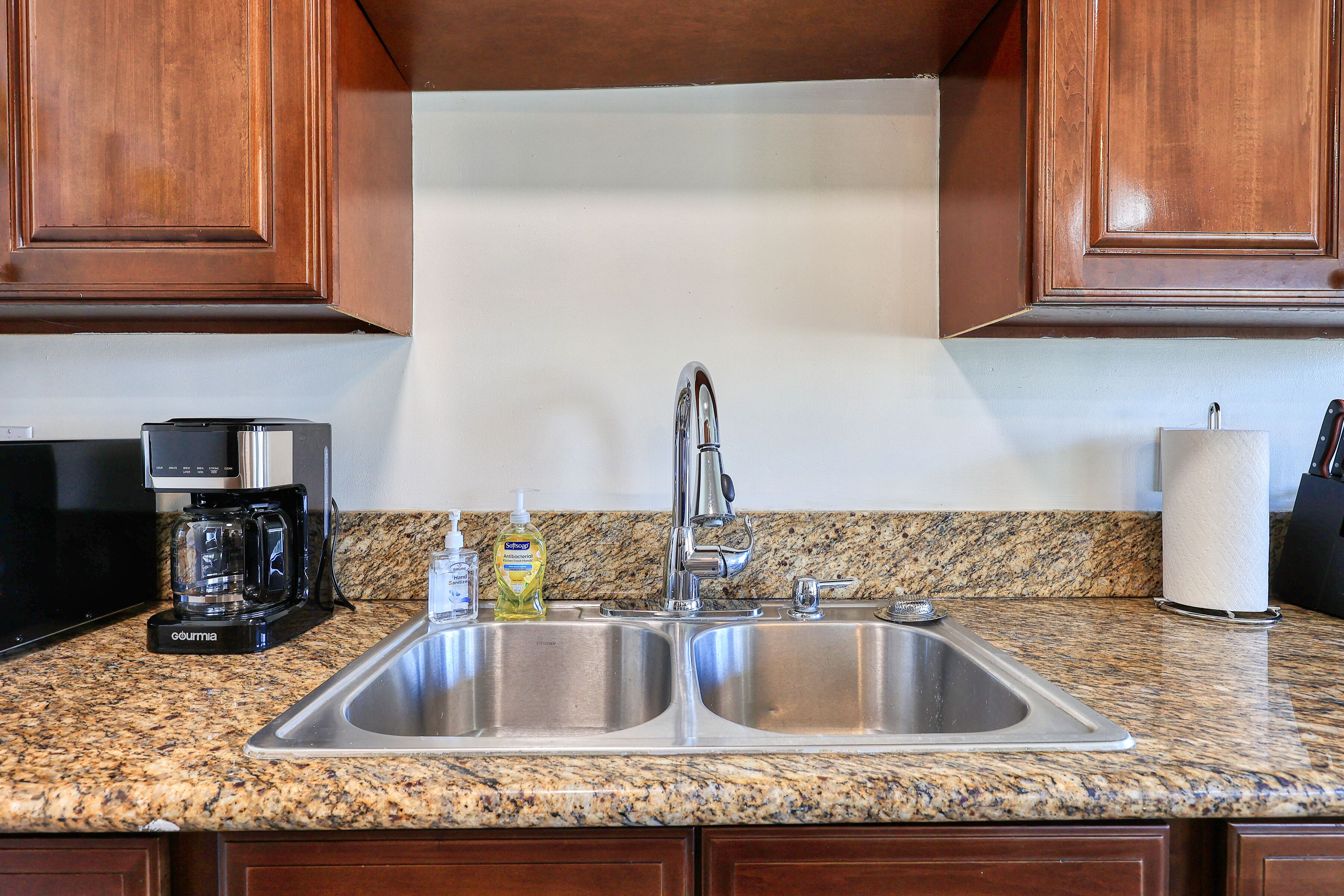 A kitchen with a double stainless steel sink, a coffee maker, and a bottle of dish soap.