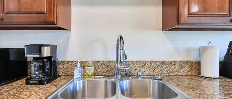 A kitchen with a double stainless steel sink, a coffee maker, and a bottle of dish soap.