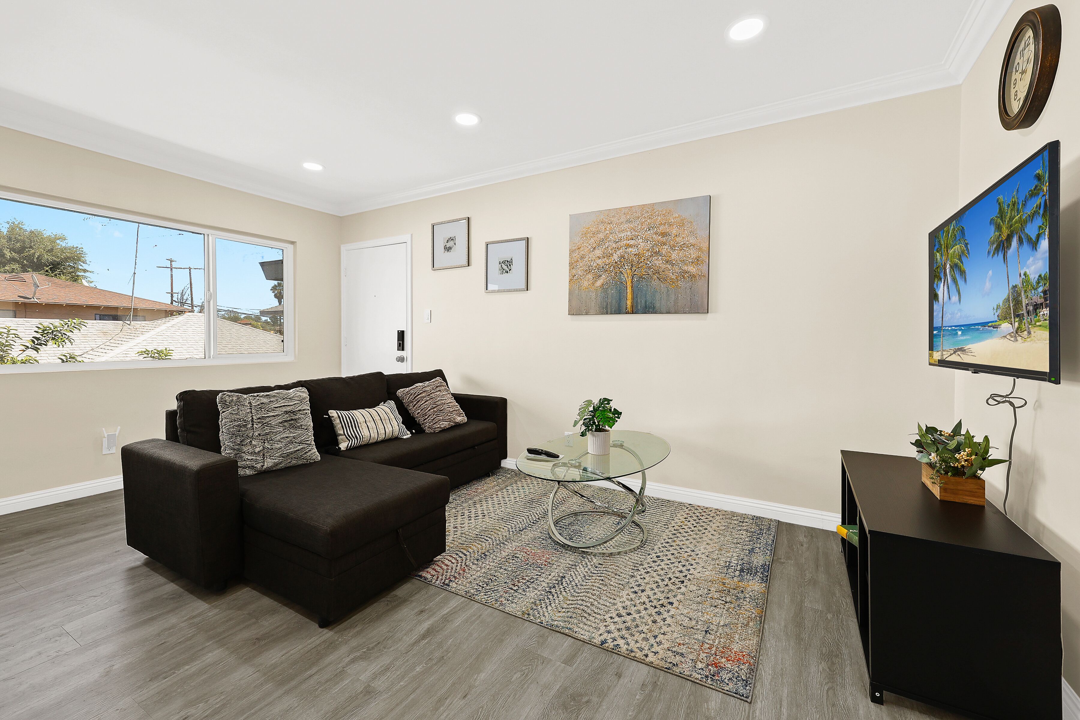 A living room with a dark brown sectional sofa, a glass coffee table, a patterned rug, and a painting of a beach scene.