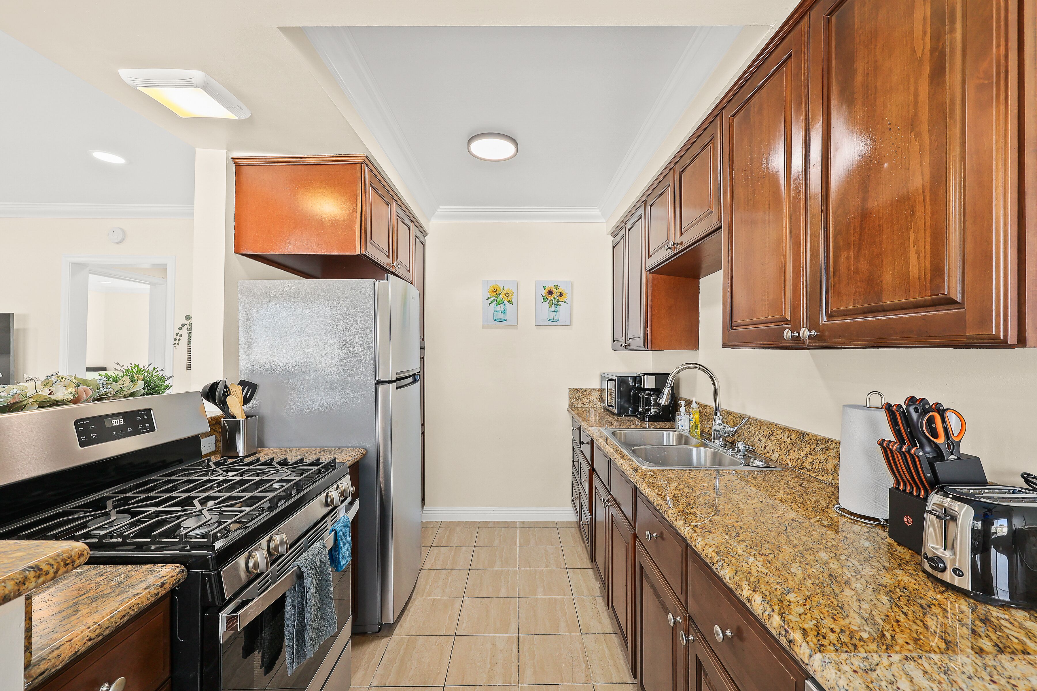 A kitchen with a stainless steel refrigerator, a gas stove, granite countertops, wooden cabinets, and a sink.