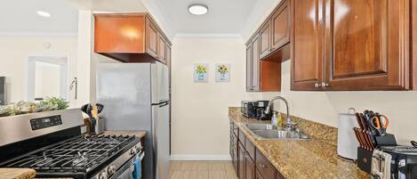 A kitchen with a stainless steel refrigerator, a gas stove, granite countertops, wooden cabinets, and a sink.
