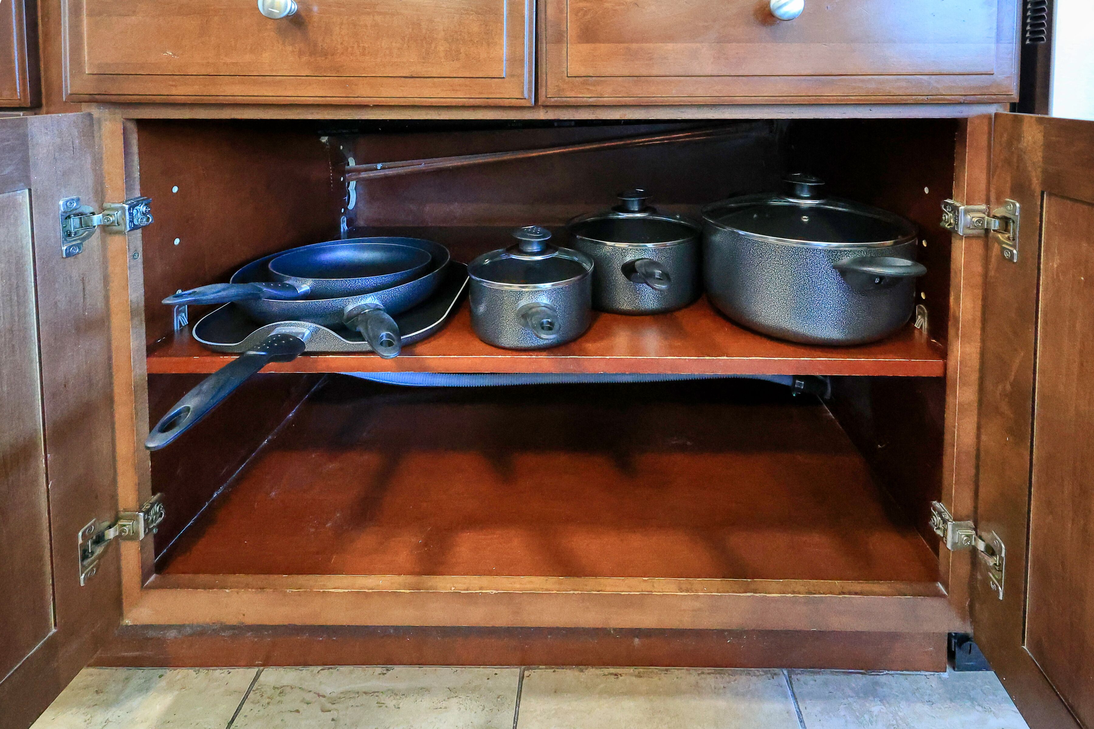Un mobiletto in legno con ripiano che contiene pentole e utensili da cucina.