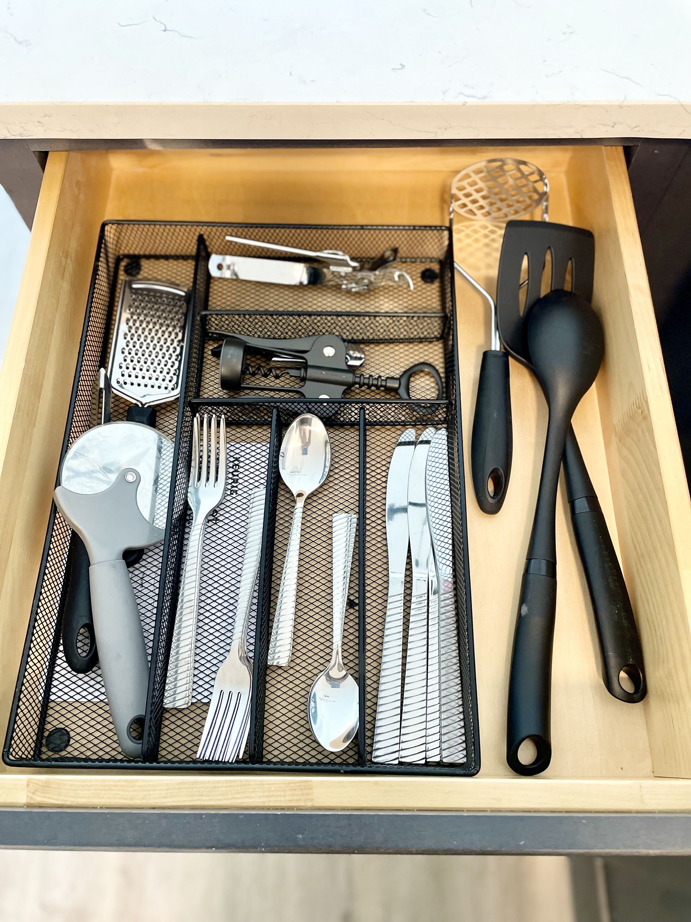 A drawer containing various kitchen utensils including a grater, spatula, and a pair of tongs.