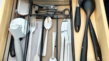 A drawer containing various kitchen utensils including a grater, spatula, and a pair of tongs.