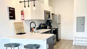 Uma cozinha moderna com uma ilha central, banquetas de bar, armários brancos, eletrodomésticos de aço inoxidável e piso de madeira.