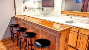 Una cocina con barra de madera, un lavamanos y tres taburetes.