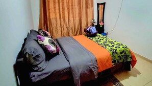 Quarto com cama, cortinas, televisão e tapete estampado.