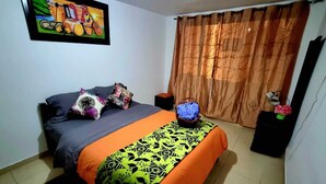 Quarto com cama, travesseiros, mesa de cabeceira, luminária e cortina.
