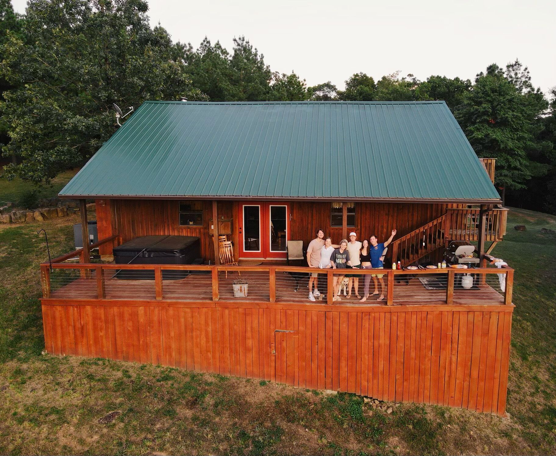 Uma cabana de madeira com telhado verde, um deck e uma área de estar externa coberta.