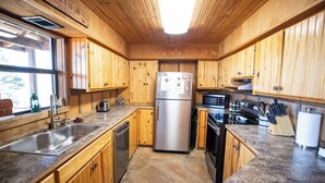 Una cocina tipo cabaña con gabinetes de madera, un refrigerador de acero inoxidable, un microondas y una estufa.