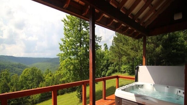 Un jacuzzi en una terraza de madera con vistas a un paisaje boscoso.