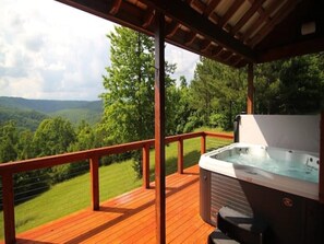 Un jacuzzi en una terraza de madera con vistas a un paisaje boscoso.