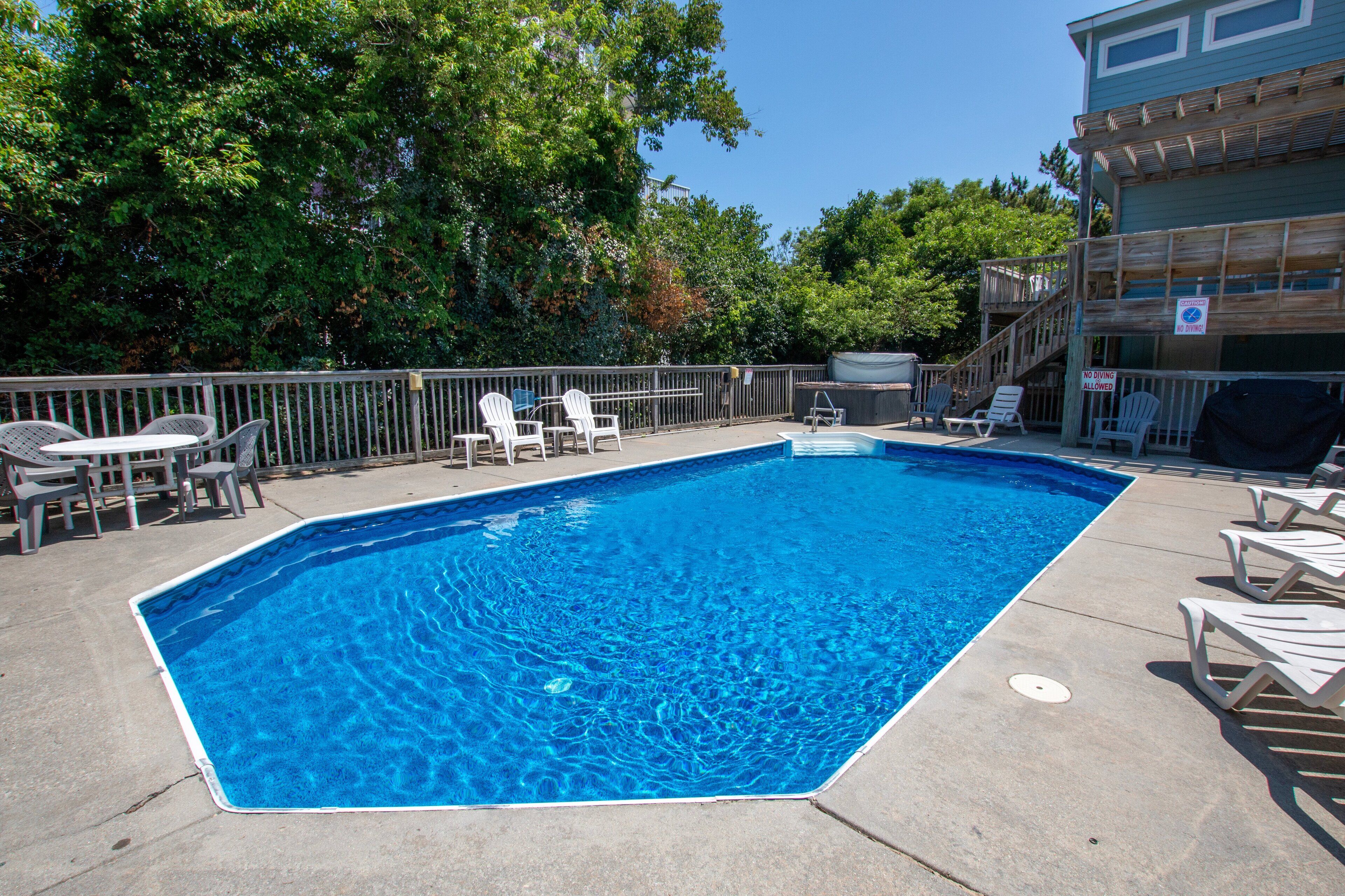 Une piscine rectangulaire, bordée d’une terrasse carrelée, entourée de chaises longues blanches et d’une clôture en métal.