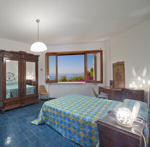 Une chambre avec un grand lit, une armoire en bois, une chaise, un bureau et une fenêtre donnant sur la mer.