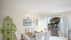 Uma sala de jantar com uma mesa posta para quatro, um armário verde e vista do jardim pela porta aberta.