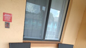 Two wicker chairs with white cushions, a window with blinds, and a red emergency instruction sign on the wall. - Clothing Optional Home Away From Home (Lutz)