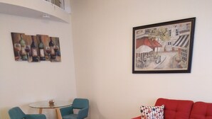A living room with a red sofa, teal chairs, a glass table, and a painting on the wall. - Clothing Optional Home Away From Home (Lutz)