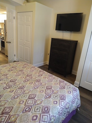 A bedroom with a bed, a television on the wall, and a door leading to another room. - Clothing Optional Home Away From Home (Lutz)