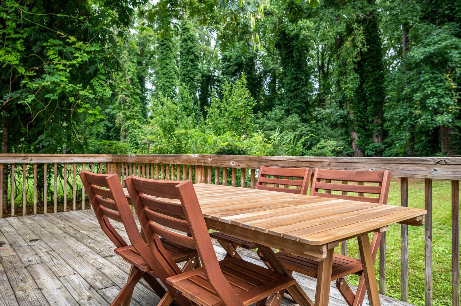 A wooden deck with a table and chairs, surrounded by dense greenery.