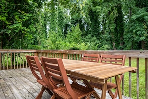 A wooden deck with a table and chairs, surrounded by dense greenery.