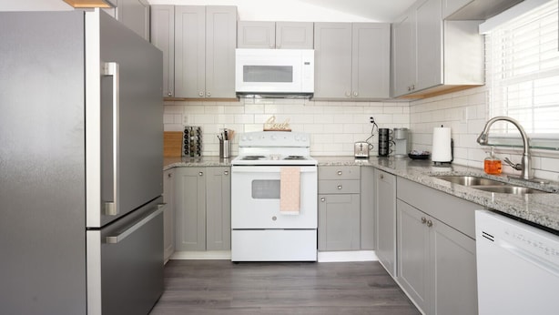 Une cuisine moderne avec des meubles gris, un réfrigérateur en acier inoxydable, un four à micro-ondes, une cuisinière et un évier.