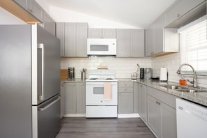 A modern kitchen with grey cabinets, a stainless steel refrigerator, a microwave, a stove, and a sink.