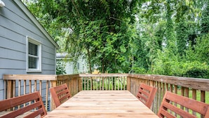 Une terrasse en bois avec une table et des chaises, entourée d’une balustrade en bois et d’arbres.