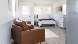 Une chambre à coucher comprenant un lit, deux fauteuils en cuir marron, une commode et un réfrigérateur.