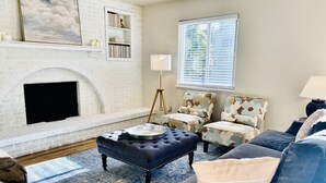 Una sala de estar con chimenea, un sofá, sillones, un tapete y una estantería.