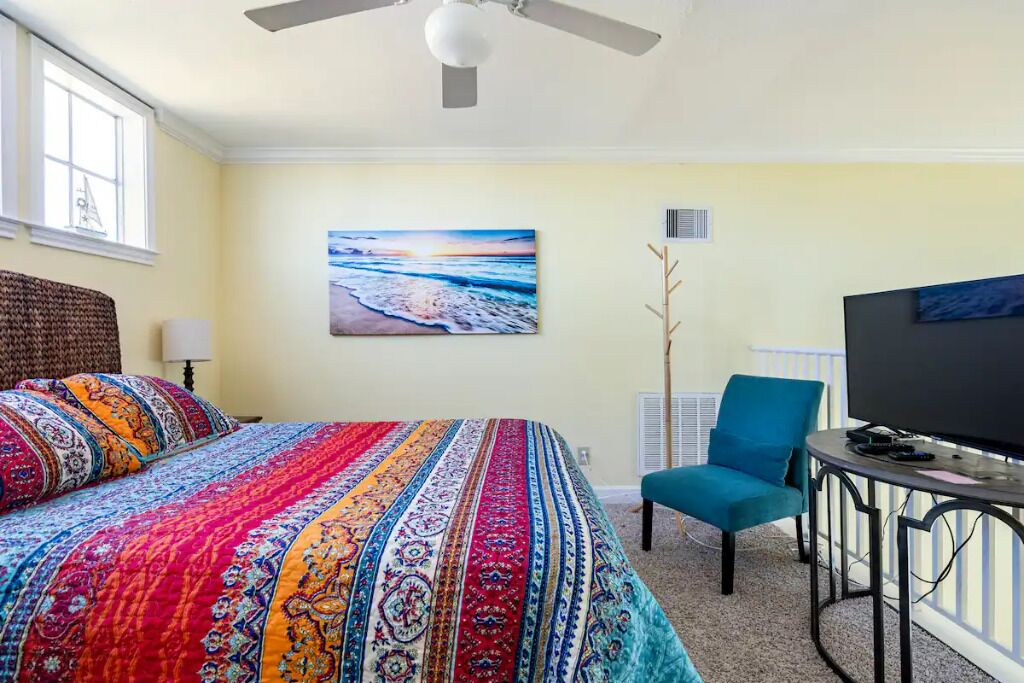 A hotel room with a large bed, a TV, a chair, and a painting of a beach scene.