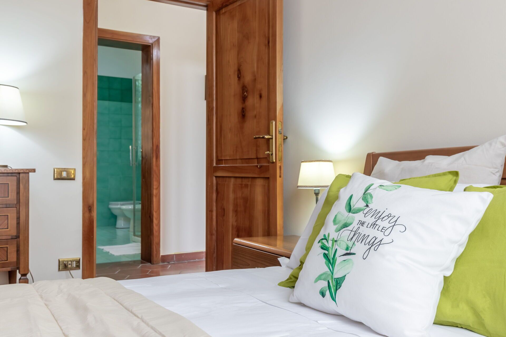 Ein Hotelzimmer mit Bett, Holztür, Badezimmer mit Duschkabine und Nachttisch mit Lampe.