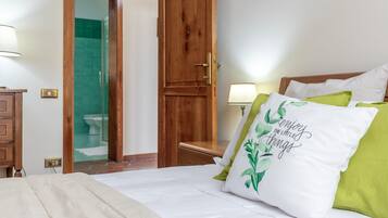 Ein Hotelzimmer mit Bett, Holztür, Badezimmer mit Duschkabine und Nachttisch mit Lampe.